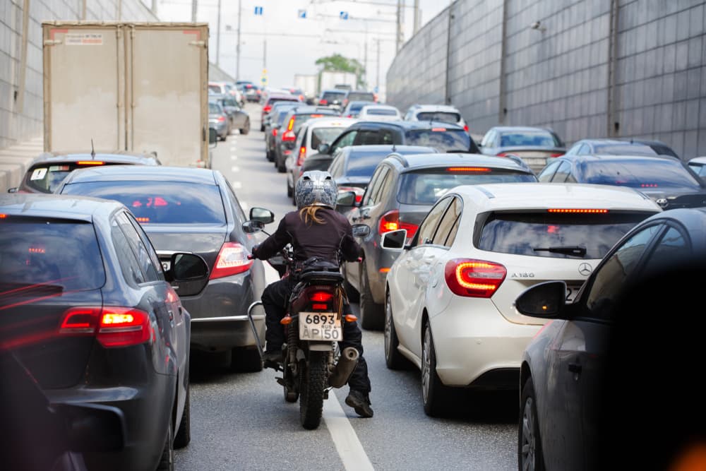 A woman on a motorcycle sneaks between the rows of cars standing in traffic.