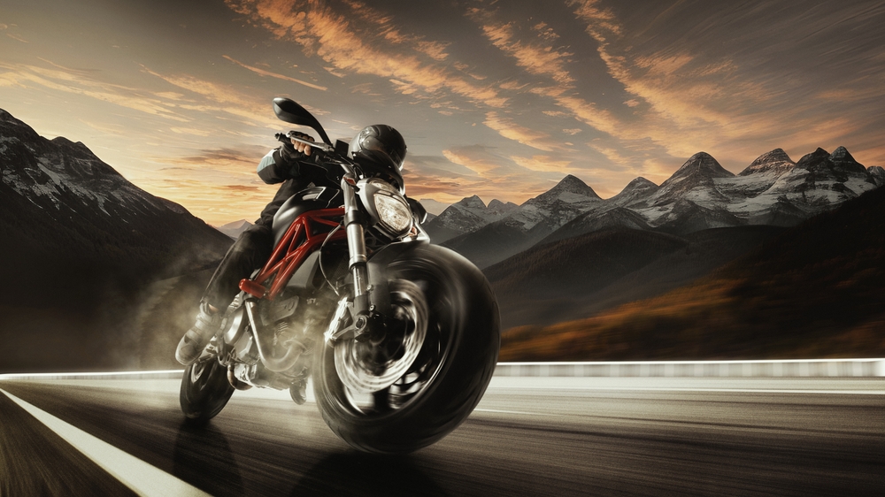 Bottom view image of a professional motorbike rider speeding around mountain roads at sunset.