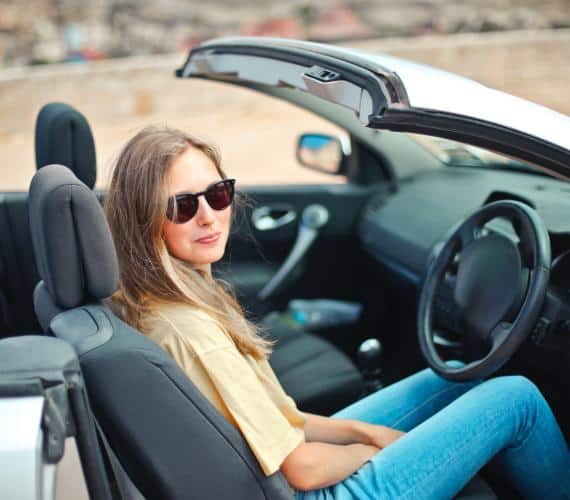 girl with sunglasses sitting in her convertible smiling
