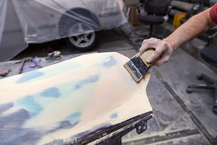 A man prepares a car body element for painting after an accident with the help of grinding abrasive paper in a car repair shop. Recovery bumper after a collision.