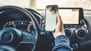 Teen driving a car while using a smartphone. Young man reading messages and holding a cell phone while driving. Risky behavior increases accident risk. Danger.