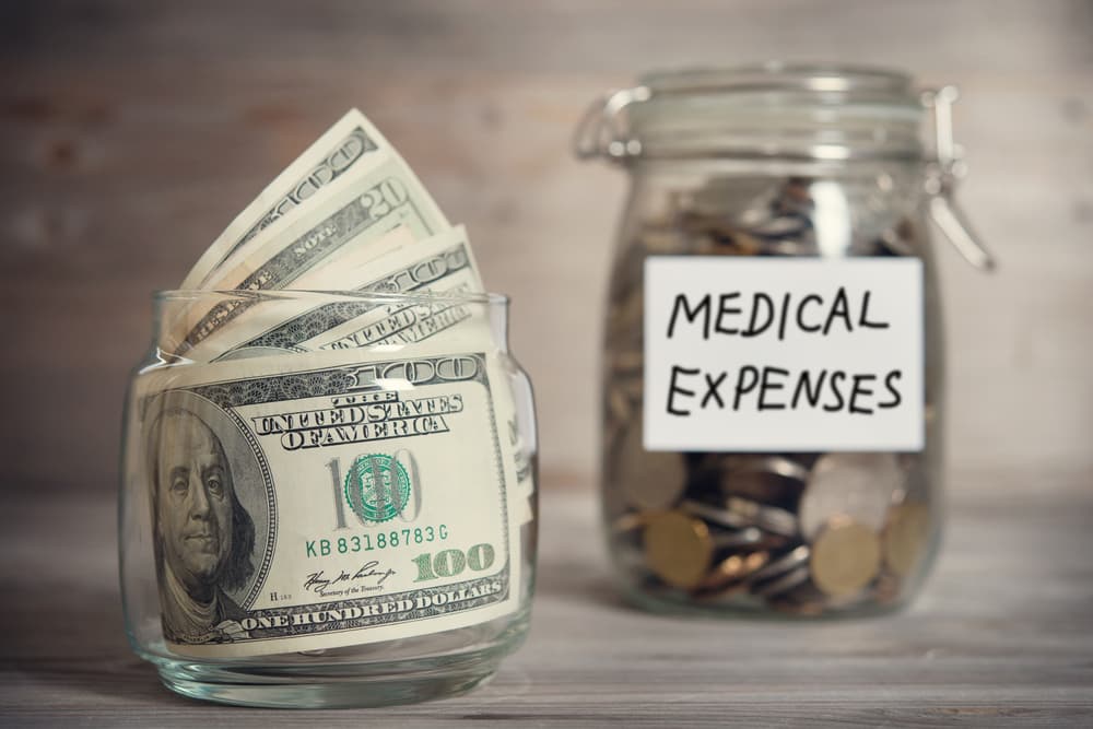 Jar labeled "Medical Expenses" filled with coins and dollars, financial concept. Wooden background with dramatic light.