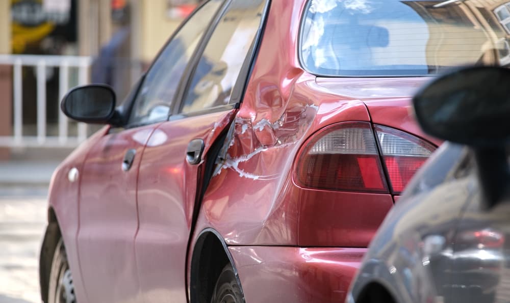 Car with a damaged body parked on a city street in Buffalo, NY, illustrating road safety and vehicle insurance issues.