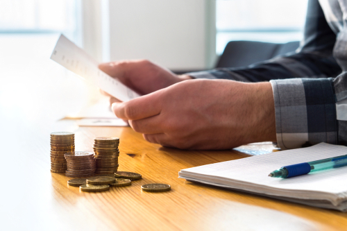 Person reviewing bills at a table with stacked coins and a pen nearby.