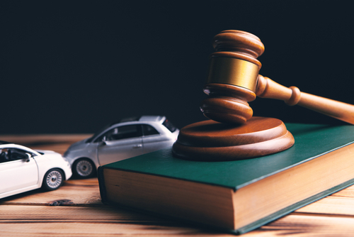 Gavel resting on a large legal book beside two toy cars, symbolizing a car accident claim.