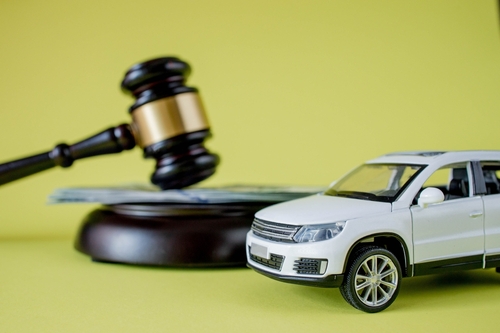 A toy white SUV sits beside a judge’s gavel with money in the background.