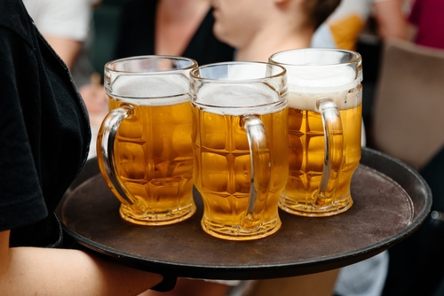 Server carrying three large mugs of beer on a tray.